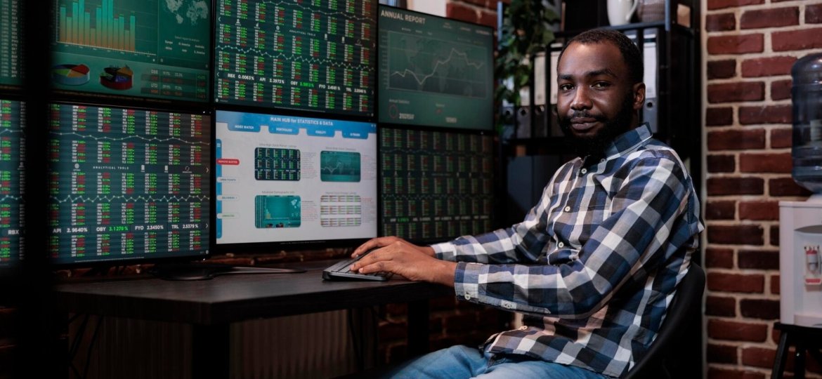 african-american-investment-company-trading-agent-sitting-workstation-desk-with-multiple-displays-looking-camera-financial-broker-trading-agency-office-with-real-time-graphs-monitors_482257-40557