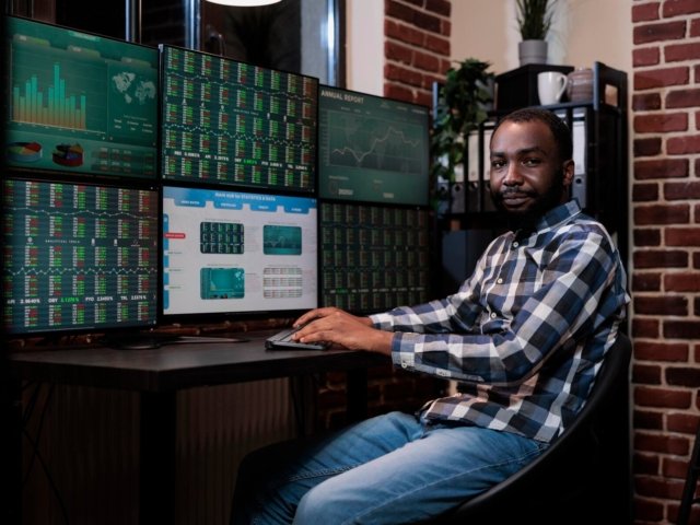 african-american-investment-company-trading-agent-sitting-workstation-desk-with-multiple-displays-looking-camera-financial-broker-trading-agency-office-with-real-time-graphs-monitors_482257-40557